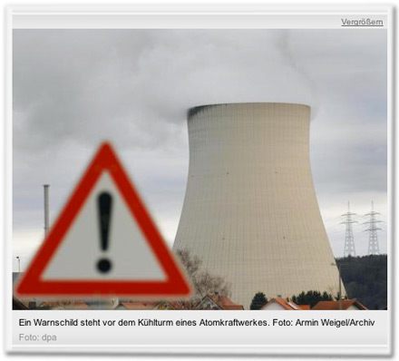 Ein Warnschild steht vor dem Kühlturm eines Atomkraftwerkes.
